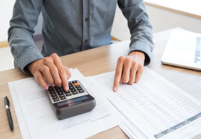 A person seated at a desk using a calculator over financial documents